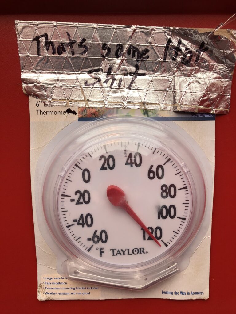A thermometer dial from the port-a-potty.  It shows a temperature of more than 120 degrees (the highest it can show).  A construction worker has labelled it with "That's some hot shit."