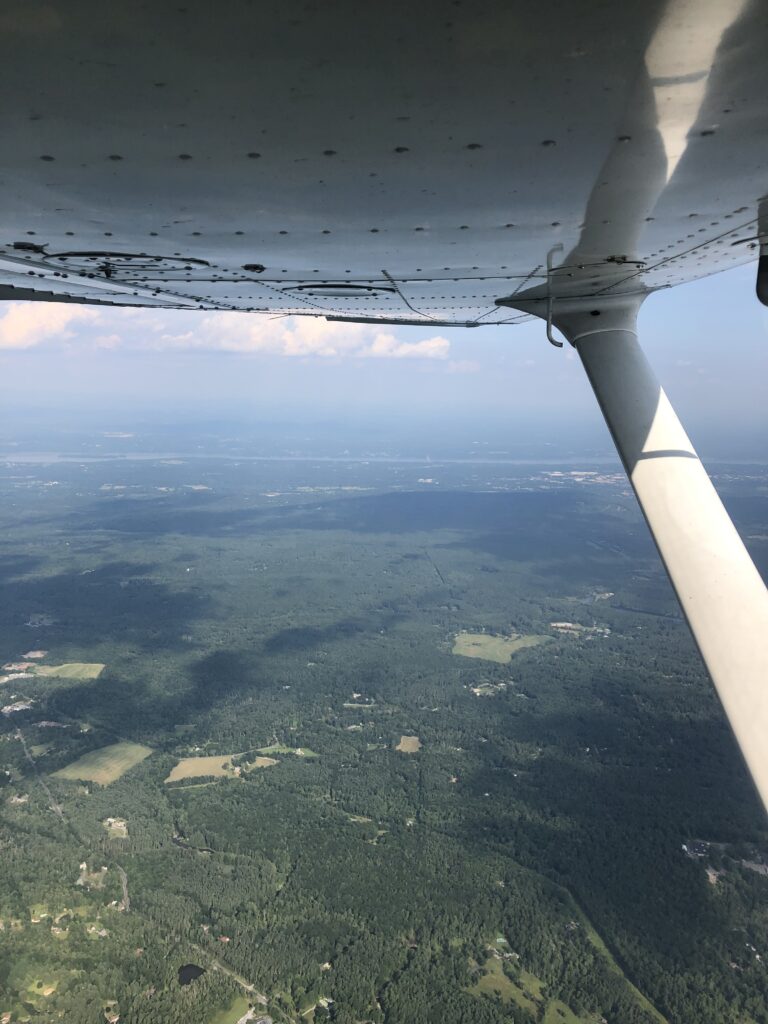 A view from the left side of the plane in flight. The Hudson river is in view in the distance.