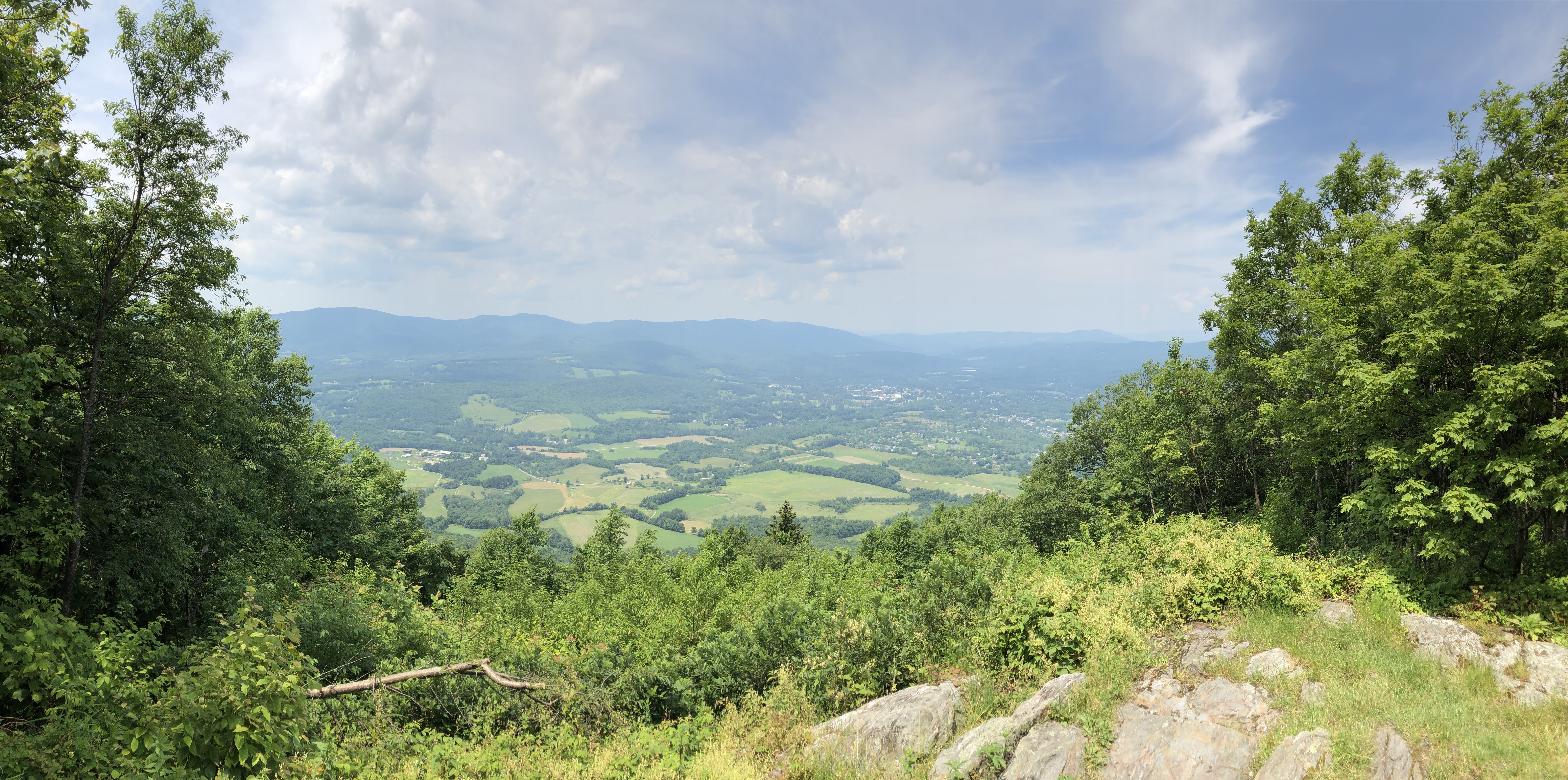 A view of the valley from the trail.  Fields appear in the valley and another mountain range is beyond.